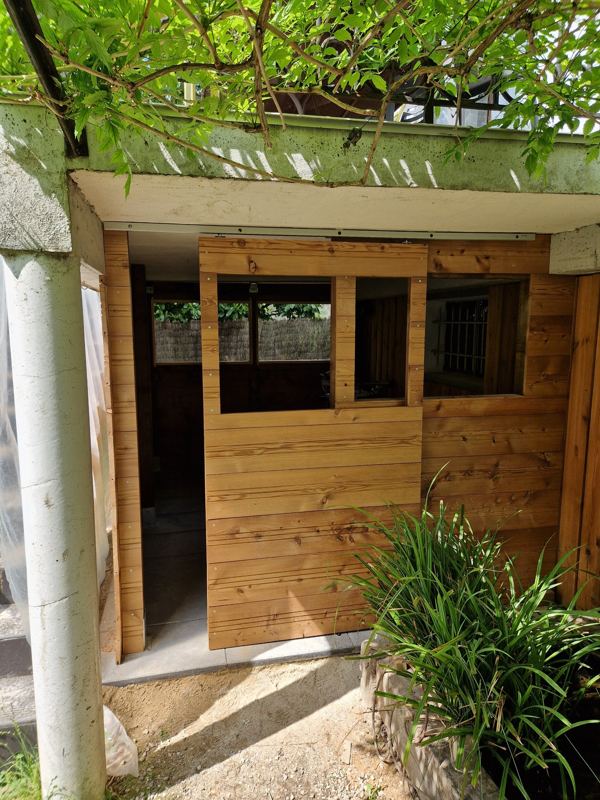 Local fermé en bardage bois sous un balcon, porte coulissante à fenêtre