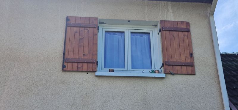 Paire de volets en bois teinté à barres et pentures noires, ouverts sur une fenêtre